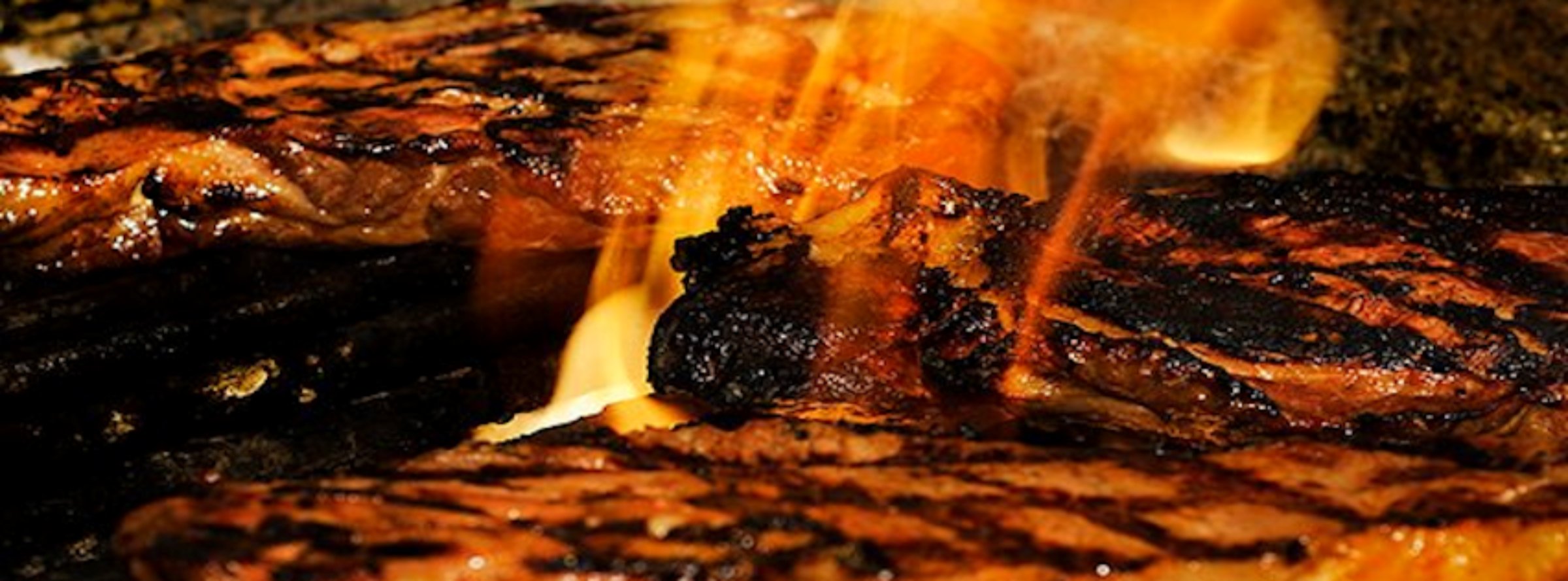 Steak grilling over an open flame at Barney Prine's